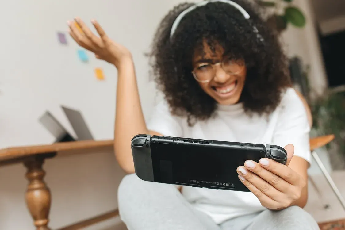 Joven con auriculares jugando sonriente a una consola portátil